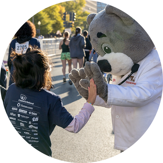 Dr. Bear mascot greeting a Race for Every Child 2025 participant who is wearing a shirt showing event sponsor logos.